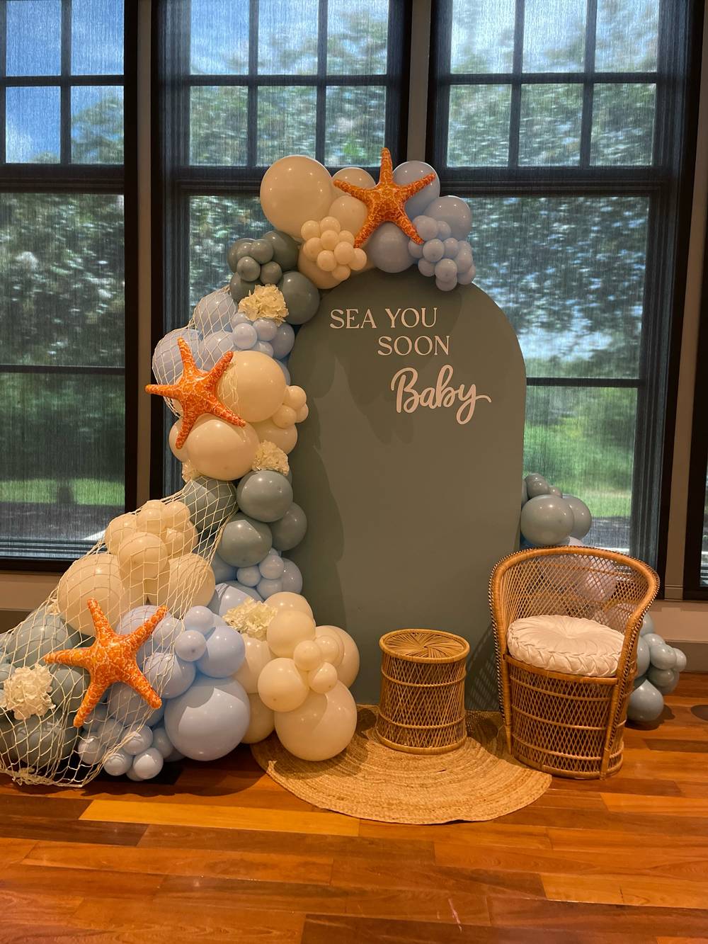 The arch panel from the side, hand lettering across its face, with the balloon garland carried over the crown and starfish worked into the cluster.